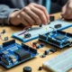 Beginner assembling an Arduino Starter Kit with a board, breadboard, LEDs, and electronic components on a desk.