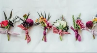 A flat lay of various trendy boutonnières in different colors and styles displayed on a white background