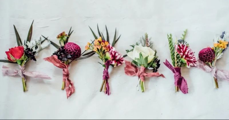 A flat lay of various trendy boutonnières in different colors and styles displayed on a white background