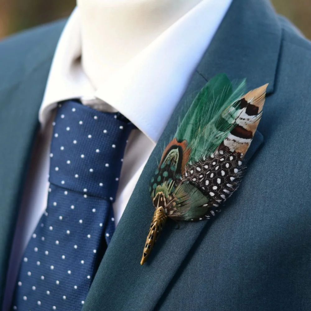 A personalized boutonnière featuring succulents, feathers, and a vintage button pinned to a leather lapel