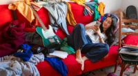 Woman relaxing on messy couch with phone and guitar nearby