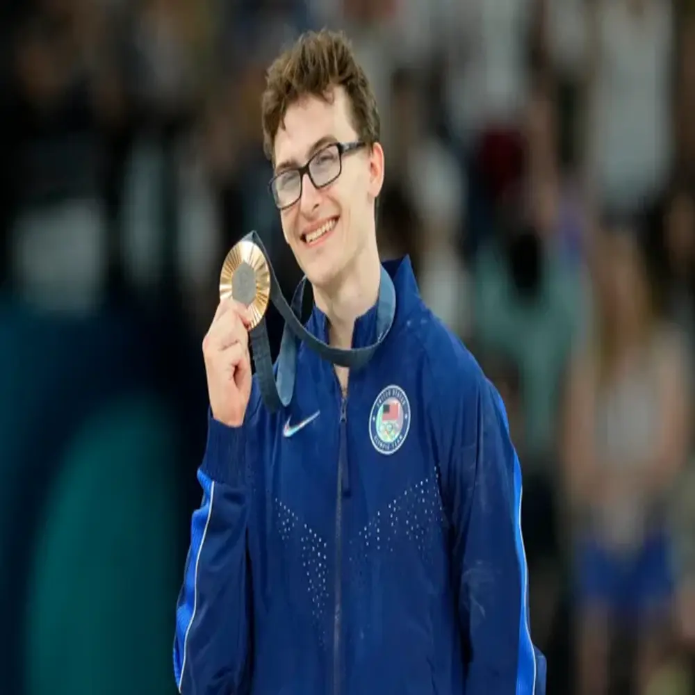 “Stephen Nedoroscik smiling and holding a medal while wearing a blue Team USA jacket, celebrating a gymnastics achievement.” 