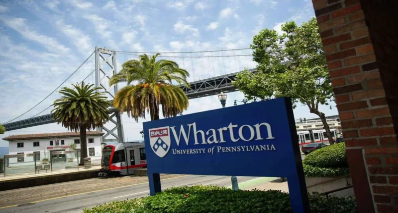 Wharton Edge at UPenn showcased through the Wharton School sign at the San Francisco campus, with palm trees, Bay Bridge, and a light rail train in the background.
