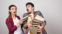 couple trying to hold a lotof books on gray wall