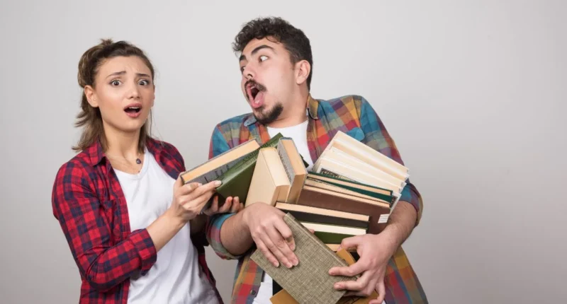 couple trying to hold a lotof books on gray wall