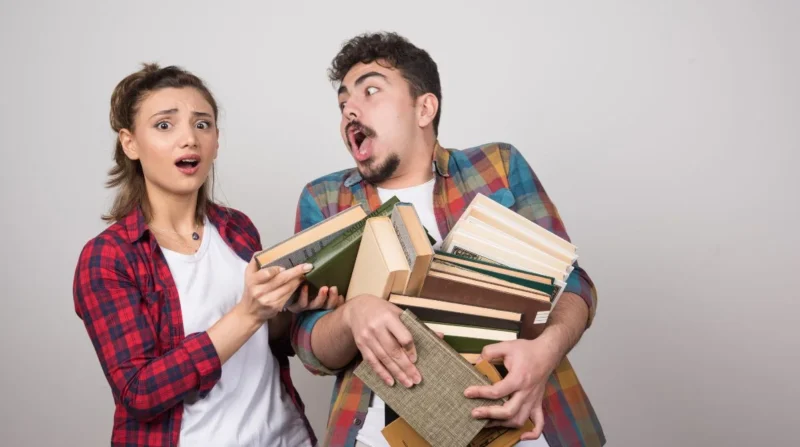 couple trying to hold a lotof books on gray wall