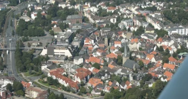 Aerial view of Hattingen showing old town rooftops, the Ruhr River, castle ruins, and surrounding green hills in warm sunset light