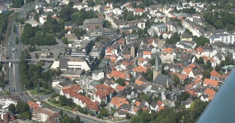 Aerial view of Hattingen showing old town rooftops, the Ruhr River, castle ruins, and surrounding green hills in warm sunset light