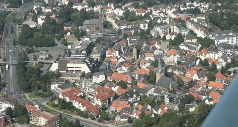 Aerial view of Hattingen showing old town rooftops, the Ruhr River, castle ruins, and surrounding green hills in warm sunset light